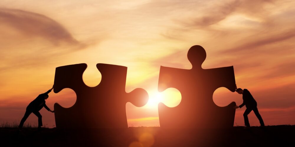 Humans pushing giant jigsaw pieces at sunset