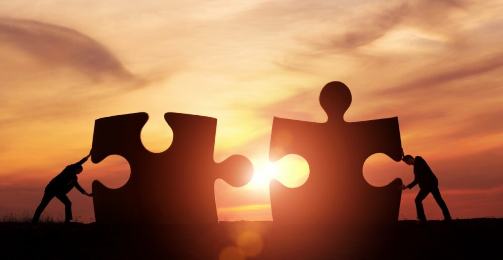 Humans pushing giant jigsaw pieces at sunset