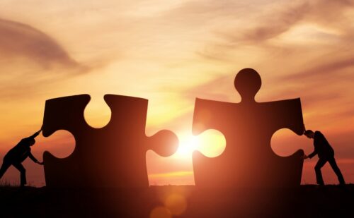 Humans pushing giant jigsaw pieces at sunset