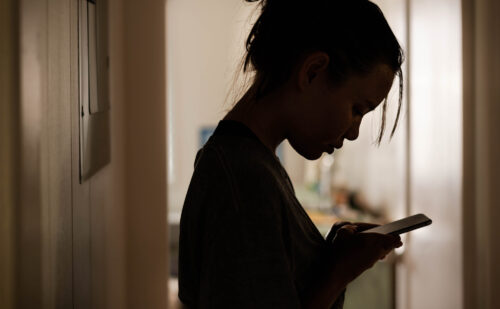 Silhouette of an upset-looking young woman viewing a message on her phone.